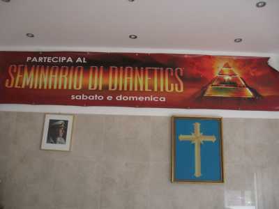 Una parete allestita con lo striscione di Dianetics, la foto di L. Ron Hubbard e la croce a otto punte simbolo di Scientology 